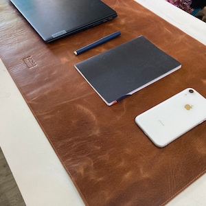 May include: A brown leather desk mat with a laptop, a notebook, a pen, and a white iPhone on it.