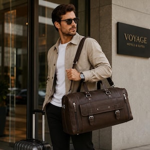 Puede incluir: Un bolso de viaje de cuero marrón oscuro con forma rectangular, que presenta un bolsillo frontal con solapa y dos cierres de hebilla, compartimentos laterales con cremallera y una correa de hombro extraíble con herrajes metálicos.