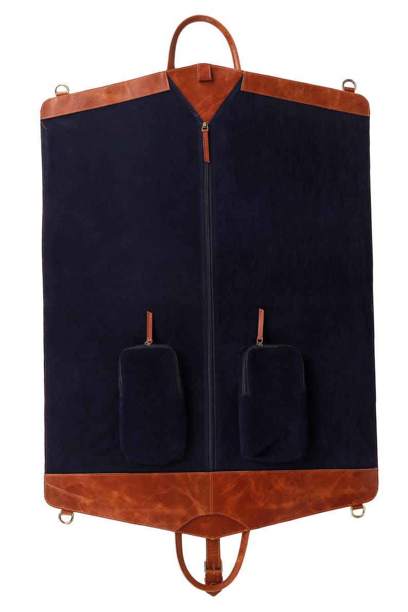 May include: A navy blue garment bag with brown leather accents. The bag features a full-length zipper, a top handle, and two small pockets. The bag has a brown leather trim at the top and bottom, with metal hardware.
