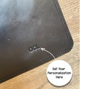 May include: Close-up of a black leather desk mat with a stitched edge. The mat has the letters "OCL" embossed in the leather.