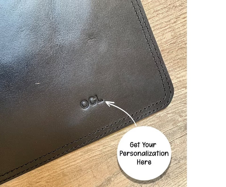 May include: Close-up of a black leather desk mat with a stitched edge. The mat has the letters "OCL" embossed in the leather.