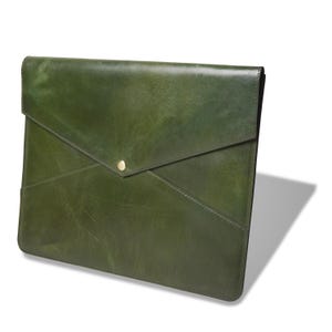 May include: A dark olive green leather document folder with an envelope-style flap closure. The folder features a smooth, slightly glossy finish and a single centred gold-toned metal snap button fastener at the point of the triangular flap.