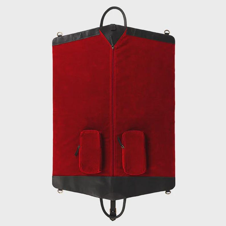 May include: A red garment bag with black leather trim and a black handle. The bag has two small pockets with zippers and a full-length zipper down the center. The bag is designed to carry clothing.