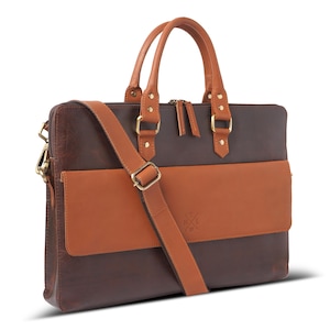 Peut inclure: Une mallette en cuir marron foncé avec une poche frontale horizontale en cuir beige clair, deux poignées assorties et une bandoulière réglable. Le sac présente des ferrures en métal doré, des fermetures éclair et un petit logo embossé.