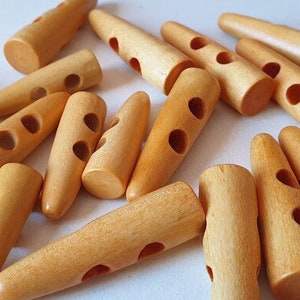 May include: A group of 15 natural wood toggle buttons with two holes each. The buttons are light brown and have a tapered shape.