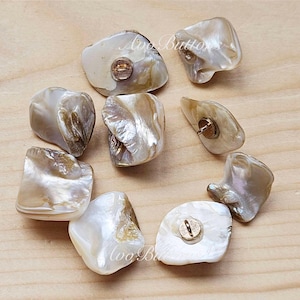 May include: Eight iridescent white and brown shell buttons with gold metal shanks. The buttons are irregular in shape and have a natural, organic look.