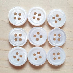 May include: Ten white, round, four-hole buttons. The buttons are made of a smooth, shiny material.