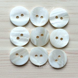 May include: Ten white round buttons with two holes each. The buttons are made of mother of pearl and have a slightly iridescent sheen.