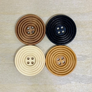 May include: Four wooden buttons with a concentric circle design. The buttons are in shades of brown, black, and white.
