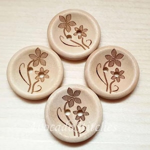 May include: Four round wooden buttons with a floral design. Each button features a light brown flower engraving with two holes for sewing. The buttons are light brown in colour and are arranged in a square.