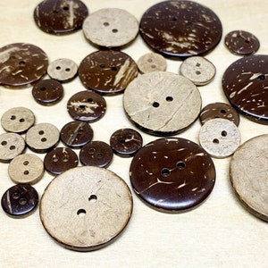 May include: A collection of brown and natural coconut shell buttons of various sizes. The buttons have two holes each and are scattered on a light wood surface.