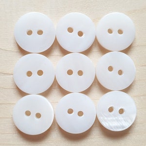 May include: Nine white round buttons, each with two holes. The buttons are made from a smooth, shiny material.