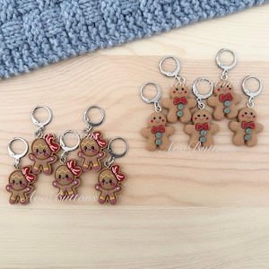 May include: A selection of gingerbread man keyrings. The keyrings feature a brown gingerbread man design with red bow ties or bows, and silver key rings. The keyrings are on a light wood surface.