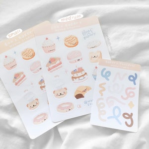 Op de afbeelding: Drie stickervellen met illustraties met een bakkerijthema. De vellen bevatten afbeeldingen van cupcakes, taarten, donuts en croissants. De tekst "Boo's Bakery" en "Bakery Confetti" is zichtbaar. De stickers zijn in pastelkleuren.