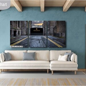 May include: A three-panel canvas print depicting a narrow street in a city. The street is lined with brick buildings and has a cobblestone surface. The middle panel features a large, arched doorway with the text "GUINNESS" above it.