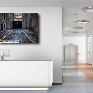 May include: A black and white photograph of a narrow street in a city. The street is lined with buildings on both sides, and there is a sign that reads "The Guinness Storehouse" at the end of the street.