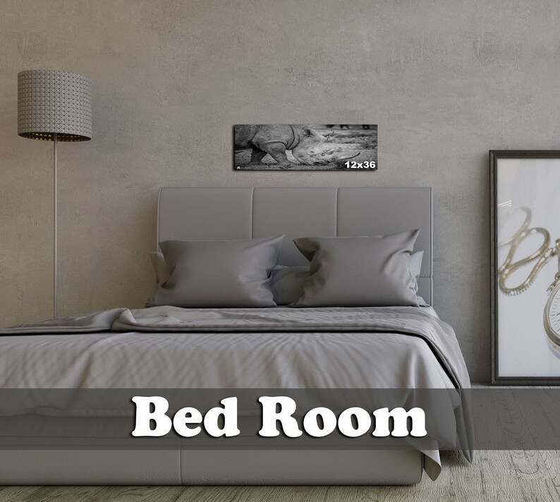 May include: A gray upholstered bed with white bedding in a bedroom setting. A black and white photograph of a rhinoceros is hanging on the wall above the bed. The photo is 12 inches by 36 inches.