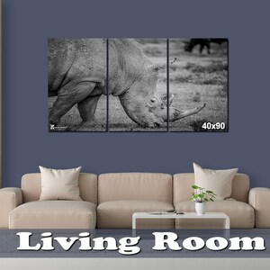 May include: A black and white photo of a rhinoceros in a three-panel canvas print. The rhinoceros is facing the left side of the image and is grazing on grass. The canvas print is 40 inches by 90 inches.
