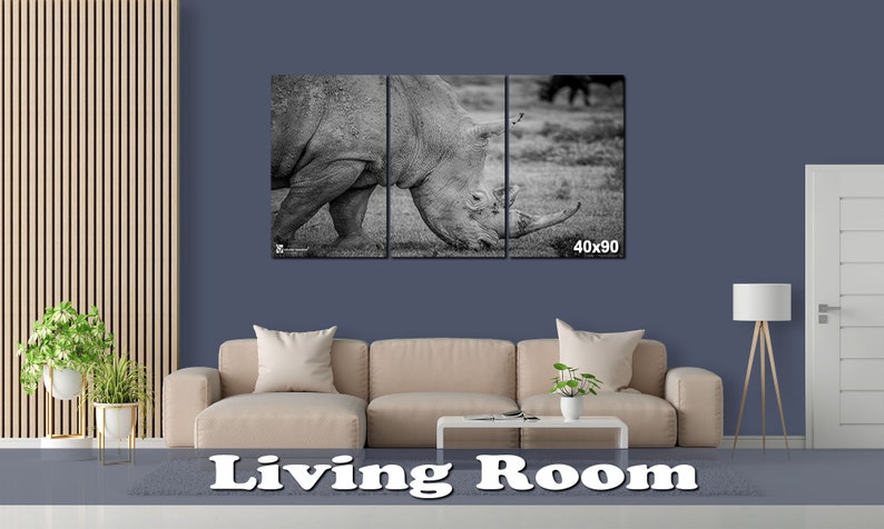 May include: A black and white photo of a rhinoceros in a three-panel canvas print. The rhinoceros is facing the left side of the image and is grazing on grass. The canvas print is 40 inches by 90 inches.