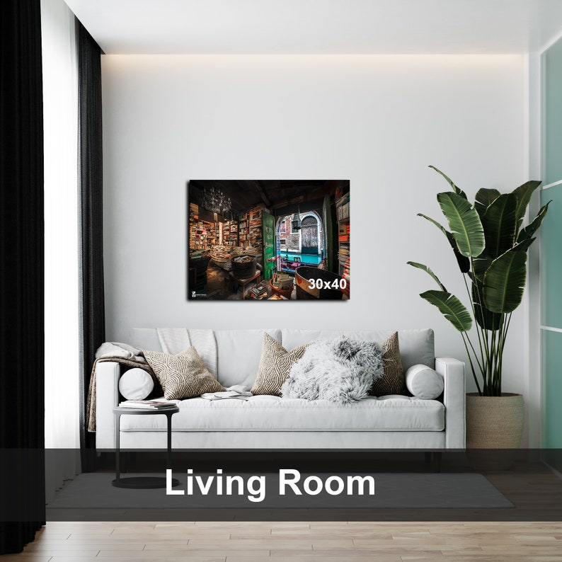May include: A white couch with pillows in a living room setting. A framed print of a bookstore interior with a window and bookshelves is hanging on the wall above the couch. The print is labeled "30x40".