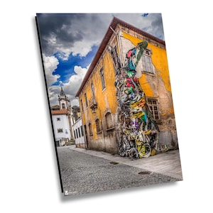 Puede incluir: Una escena callejera con un gran mural colorido de un conejo pintado en el lateral de un edificio amarillo. La obra de arte es detallada y vibrante, contrastando con la fachada envejecida. Una calle adoquinada conduce a una iglesia en la distancia.