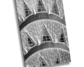 May include: Black and white photograph of the Chrysler Building in New York City. The image shows the unique art deco design of the building's facade, featuring a series of repeating geometric patterns and windows.