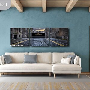 May include: A three-panel canvas print depicting a city street scene with a brick archway and a cobblestone road. The print is displayed on a white couch in a living room setting.