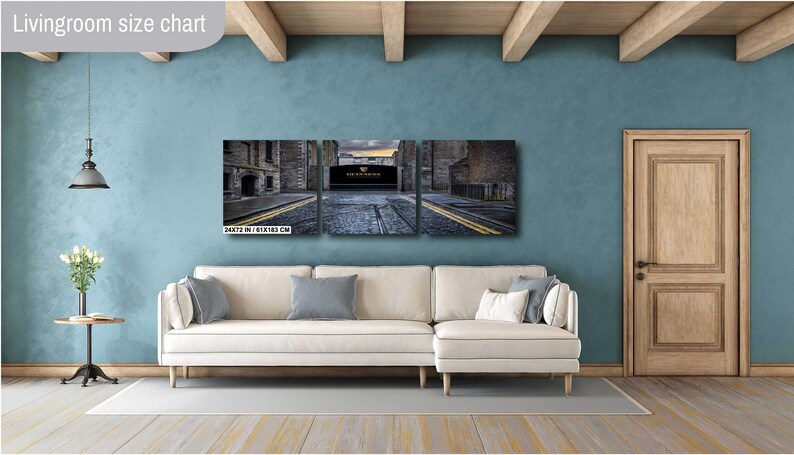 May include: A three-panel canvas print depicting a city street scene with a brick archway and a cobblestone road. The print is displayed on a white couch in a living room setting.