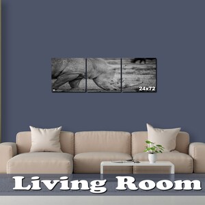 May include: A black and white photograph of a rhinoceros in a living room setting. The photo is split into three panels and is hung above a beige couch. The photo is 24 inches by 72 inches.