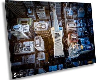 May include: An aerial view of a city skyline with a tall, white, modern skyscraper in the center. The skyscraper is surrounded by other buildings, some of which are taller than others. The buildings are all different shapes and sizes, and they are all made of different materials. The sky is blue and the sun is shining.