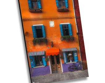 Può includere: Un edificio arancione brillante con finestre blu e un baldacchino rosso sopra l'ingresso. Una bicicletta è parcheggiata davanti all'edificio.