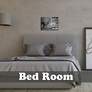 May include: A gray upholstered bed with a white duvet cover and two pillows. A black and white photo of a rhinoceros is hanging on the wall above the bed. The photo is labeled "16x20". The text "Bed Room" is printed in white on a gray background at the bottom of the image.