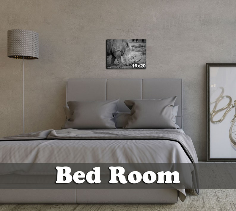 May include: A gray upholstered bed with a white duvet cover and two pillows. A black and white photo of a rhinoceros is hanging on the wall above the bed. The photo is labeled "16x20". The text "Bed Room" is printed in white on a gray background at the bottom of the image.