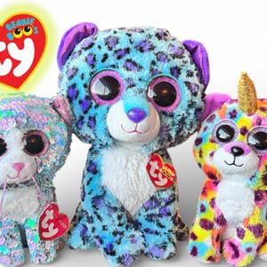 Może przedstawiać: Trzy kolorowe pluszaki Beanie Boos. Pluszaki obejmują niebieskiego lamparta z fioletowymi plamami, wielokolorowego jednorożca-lamparta i pluszaka z cekinami. Każda zabawka ma duże, błyszczące oczy i metkę w kształcie serca.