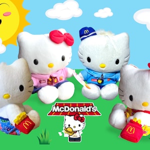 May include: Four white plush Hello Kitty dolls, each with different outfits and accessories, are arranged on a green surface with a blue sky background. The McDonald's logo is visible. One doll holds a red fry container.