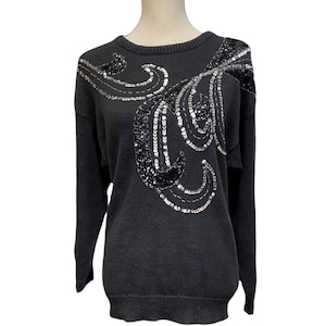 Può includere: Maglione nero con un design di paillettes argento e nero. Il design presenta una serie di linee e forme curve.
