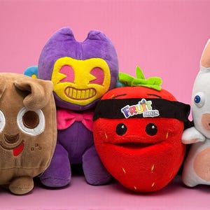 Può includere: Quattro peluche sono disposti in fila su uno sfondo rosa. I giocattoli includono un cane marrone, un personaggio viola con una faccia gialla, una fragola rossa con una fascia nera e un coniglio bianco.