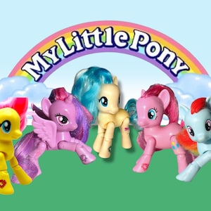 Op de afbeelding: Vijf My Little Pony figuren met beweegbare ledematen, regenboogvleugels en kleurrijk haar. De pony's zijn geel, roze, lichtblauw, paars en blauw. De figuren zijn speels geposeerd. De achtergrond heeft een regenboog en wolken.