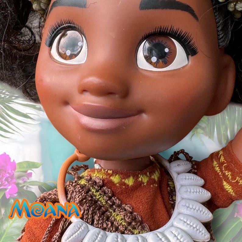 Close-up of Moana’s face, showing her large brown eyes, gentle smile, and white shell necklace. Her handmade dress and curly hair are partially visible.