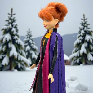 Side profile of Anna Frozen II doll showing auburn hair bun, layered cape colors, and dress details