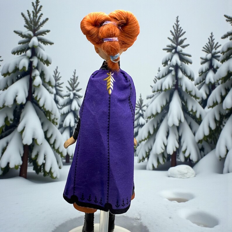 Back view of Anna doll showing purple cape with stitched edging and gold leaf symbol near collar