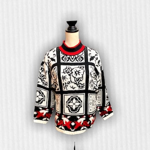 May include: A black and white patterned sweater with a red trim around the neck. The sweater has a geometric design with various shapes and symbols.