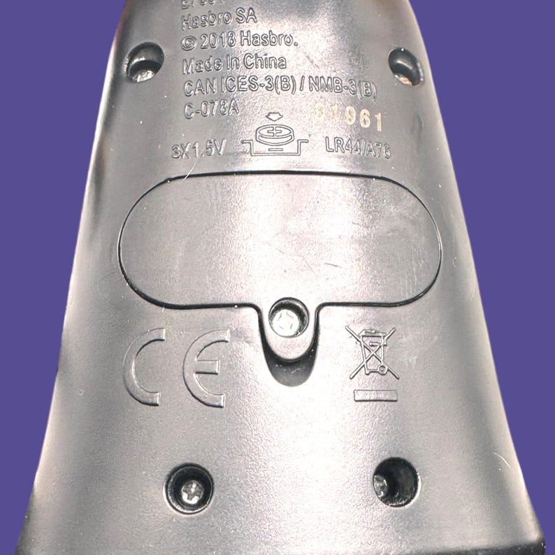 Close-up of back of doll showing Hasbro markings, battery compartment, and battery type information