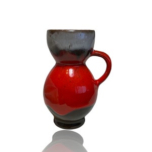 Puede incluir: Un jarrón de cerámica rojo y negro con una base ancha y un asa. El jarrón tiene un acabado esmaltado y una forma única.