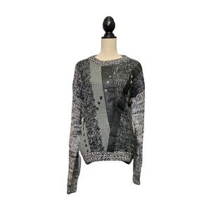 May include: A grey and black knitted jumper with a black leather panel and heart-shaped details.
