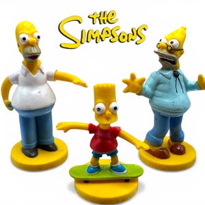 May include: Three Simpsons character figurines: Homer, Bart on a skateboard, and another Homer figure. The Simpsons logo is in yellow above the figures. Homer wears a white shirt and blue trousers. Bart wears a red top and blue shorts. The figures stand on yellow bases.