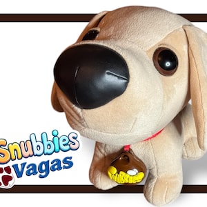 May include: A beige plush dog toy with a black nose and brown eyes. The dog is wearing a red collar with a brown tag that says "Snubbies".
