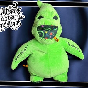 Può includere: Peluche verde del personaggio "Oogie Boogie" del film "Nightmare Before Christmas". Il giocattolo ha una bocca cucita con una maschera a motivi colorati e una lingua a strisce nere e arancioni.