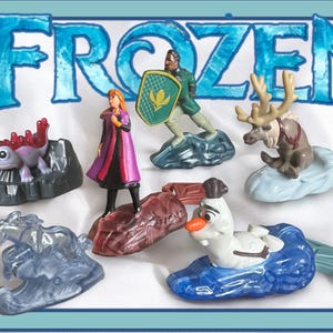 Op de afbeelding: Een set van zes Frozen-personage speelgoed. Het speelgoed is gemaakt van plastic en bevat Elsa, Anna, Kristoff, Olaf, Sven en Hans. Het speelgoed is allemaal in hun kenmerkende kleuren en heeft gedetailleerde kenmerken. Het speelgoed is verpakt in een doorzichtige plastic zak met een Frozen-logo.
