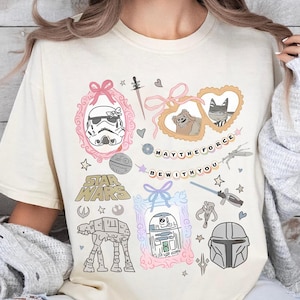 Retro pastel water color coquette Star Wars shirt with kawaii-style Stormtrooper, R2D2, AT-AT, Ewok, and Mandalorian helmet in watercolor frames with bows and hearts, perfect for Disney trip or Star Wars Day outfit.